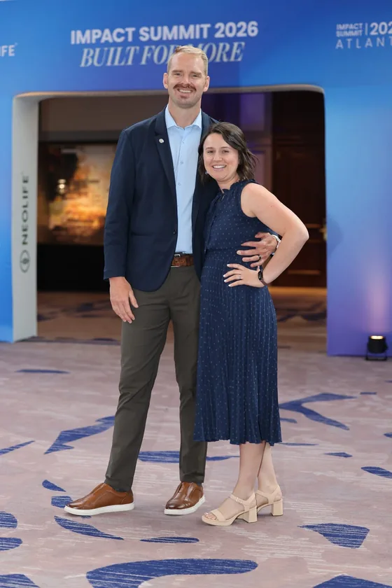 Joseph Cordes and his wife smiling together in front of the Impact Summit 2026 stage entrance